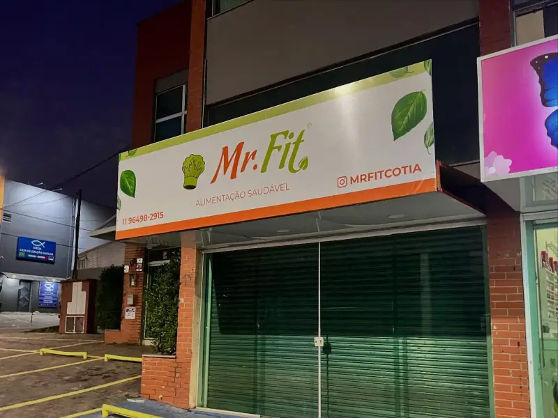 Fachada com painel impresso do restaurante de alimentação saudável Mr.Fit em Cotia ao anoitecer