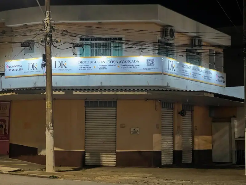 Fachada de esquina iluminada da clínica DK Dentista e Estética Avançada com painéis contornando o prédio