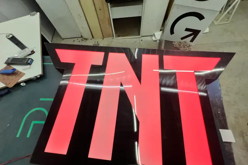 Luminoso TNT em acrílico vermelho aceso visto de cima na bancada da oficina