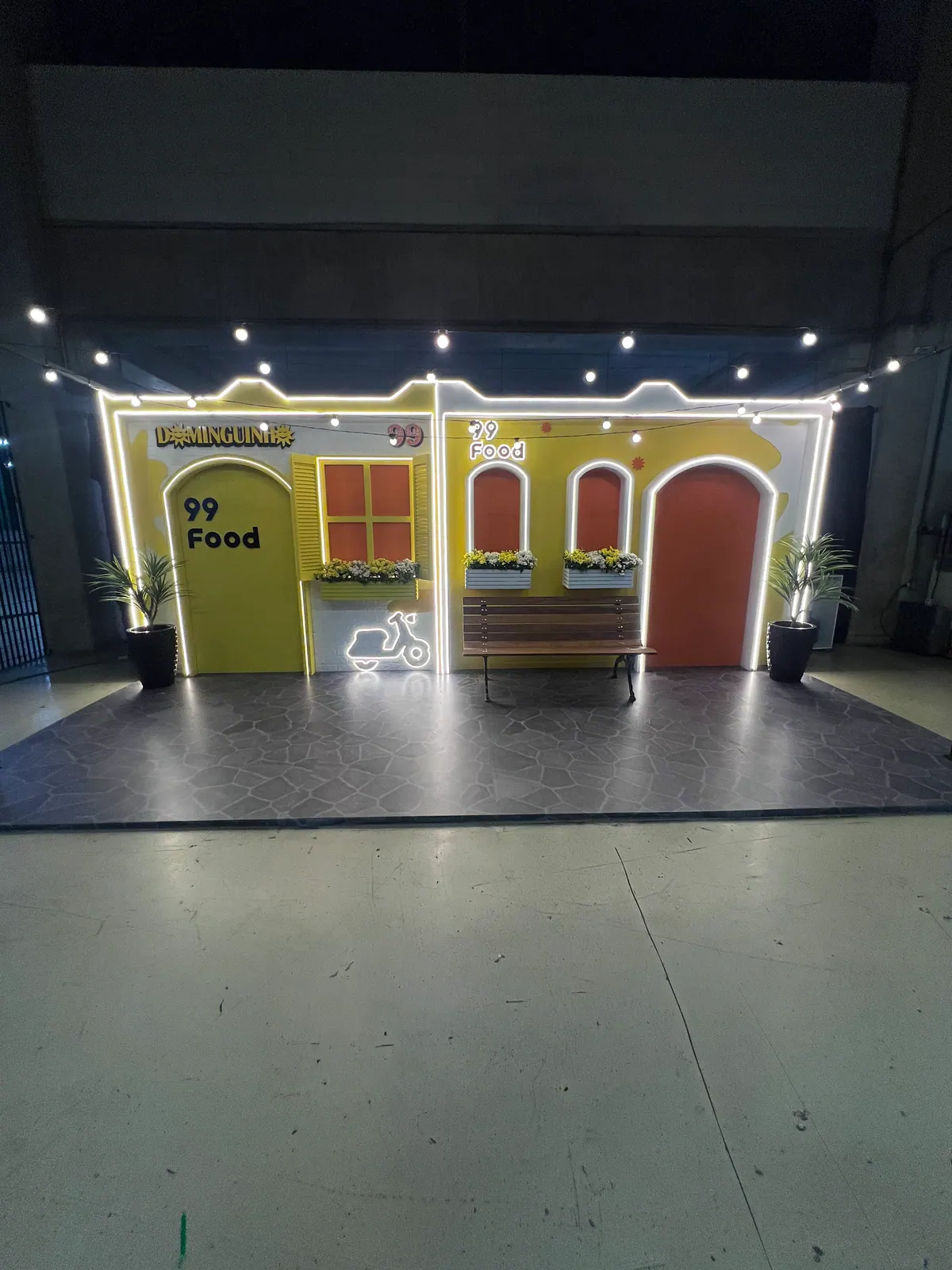 Casinha cenográfica da ativação 99Food com contorno de neon e banco de praça — foto 1