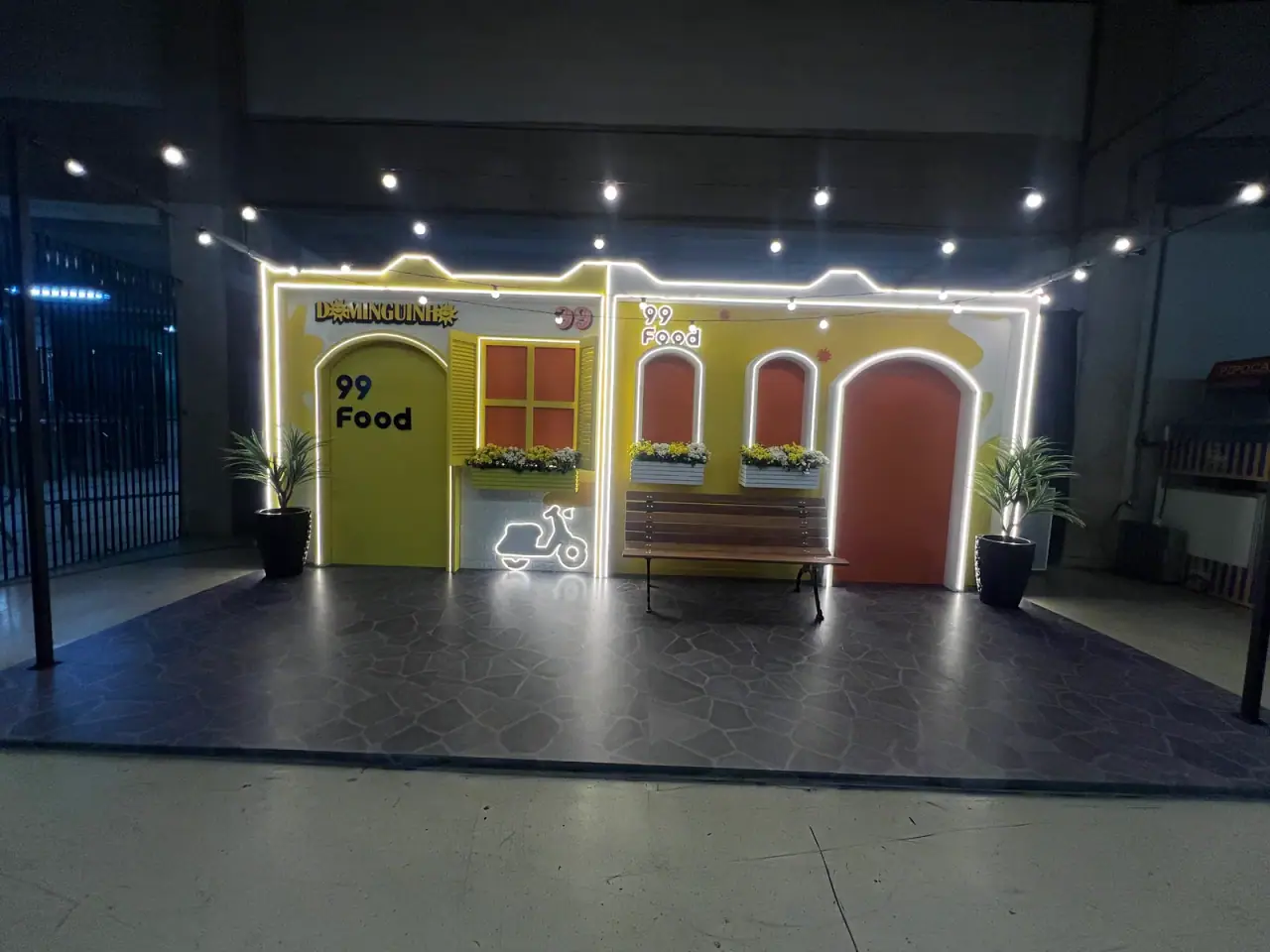 Casinha cenográfica da ativação 99Food com contorno de neon e banco de praça — foto 2