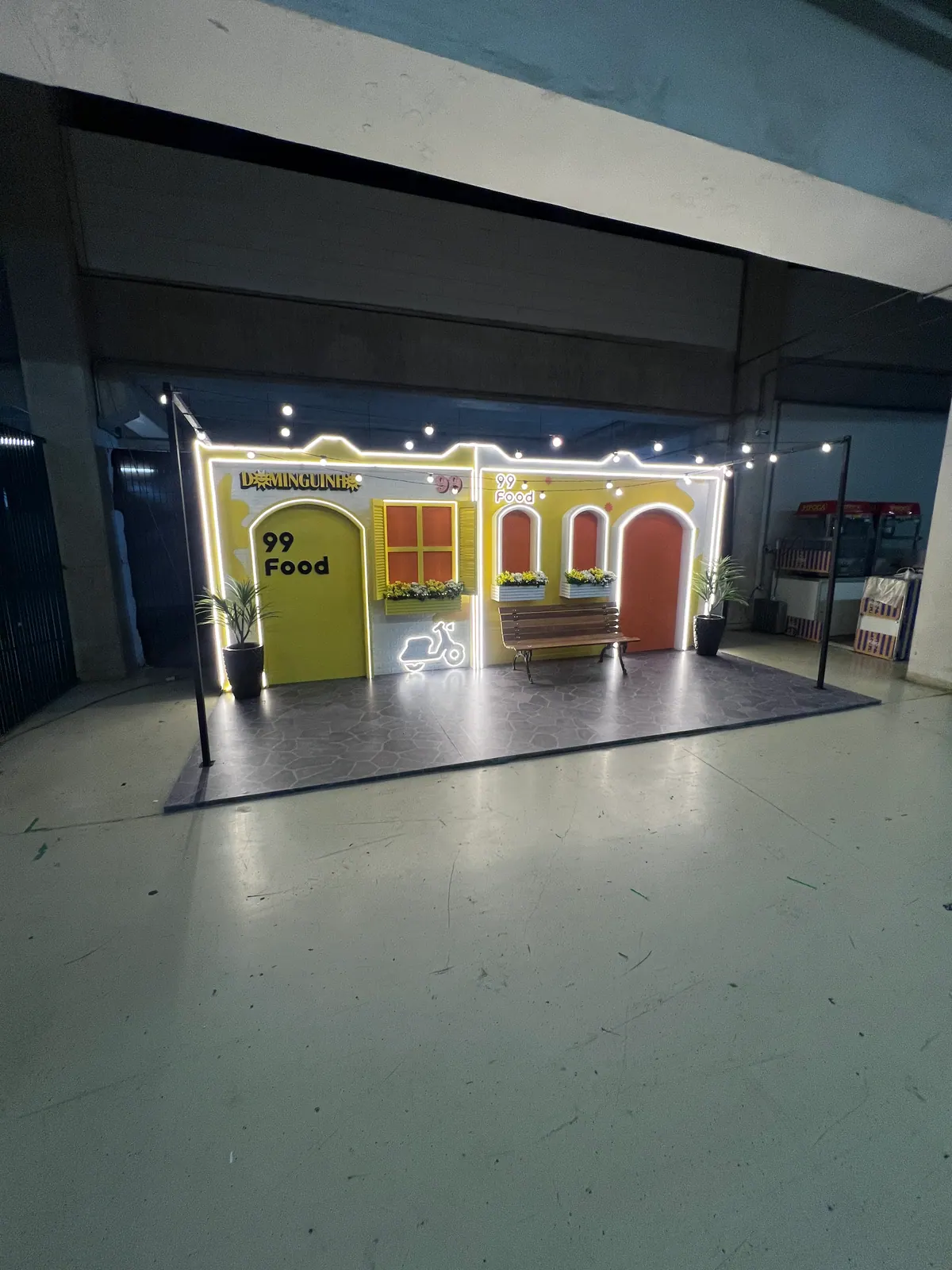 Casinha cenográfica da ativação 99Food com contorno de neon e banco de praça — foto 3