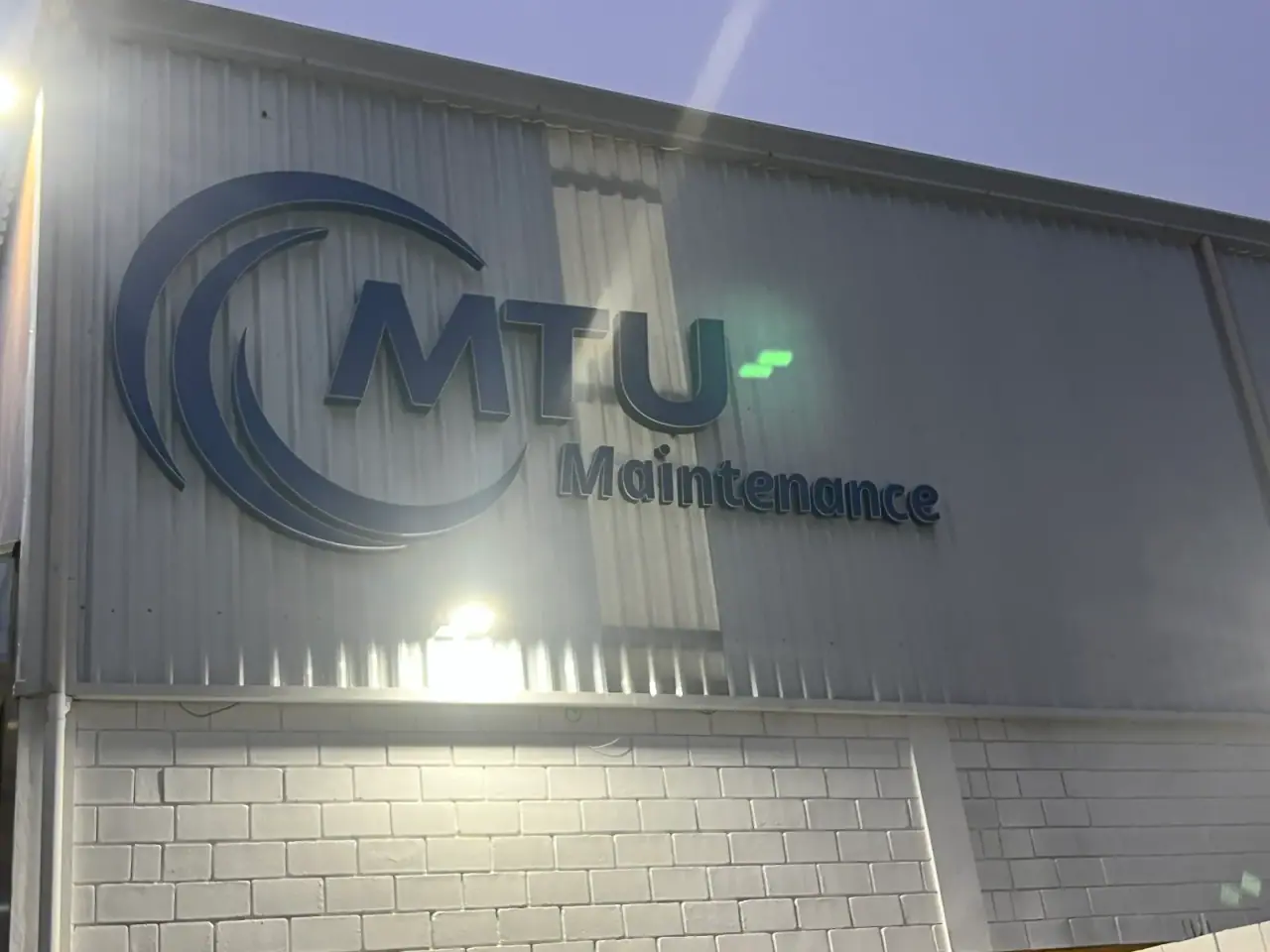 Letreiro iluminado da MTU Maintenance em galpão industrial — foto 1