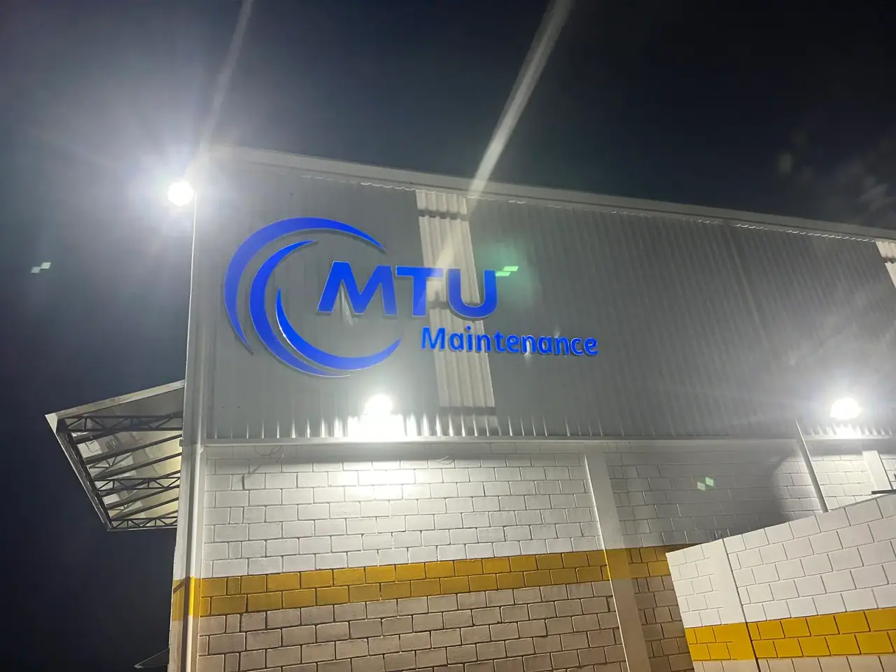 Letreiro iluminado da MTU Maintenance em galpão industrial — foto 2