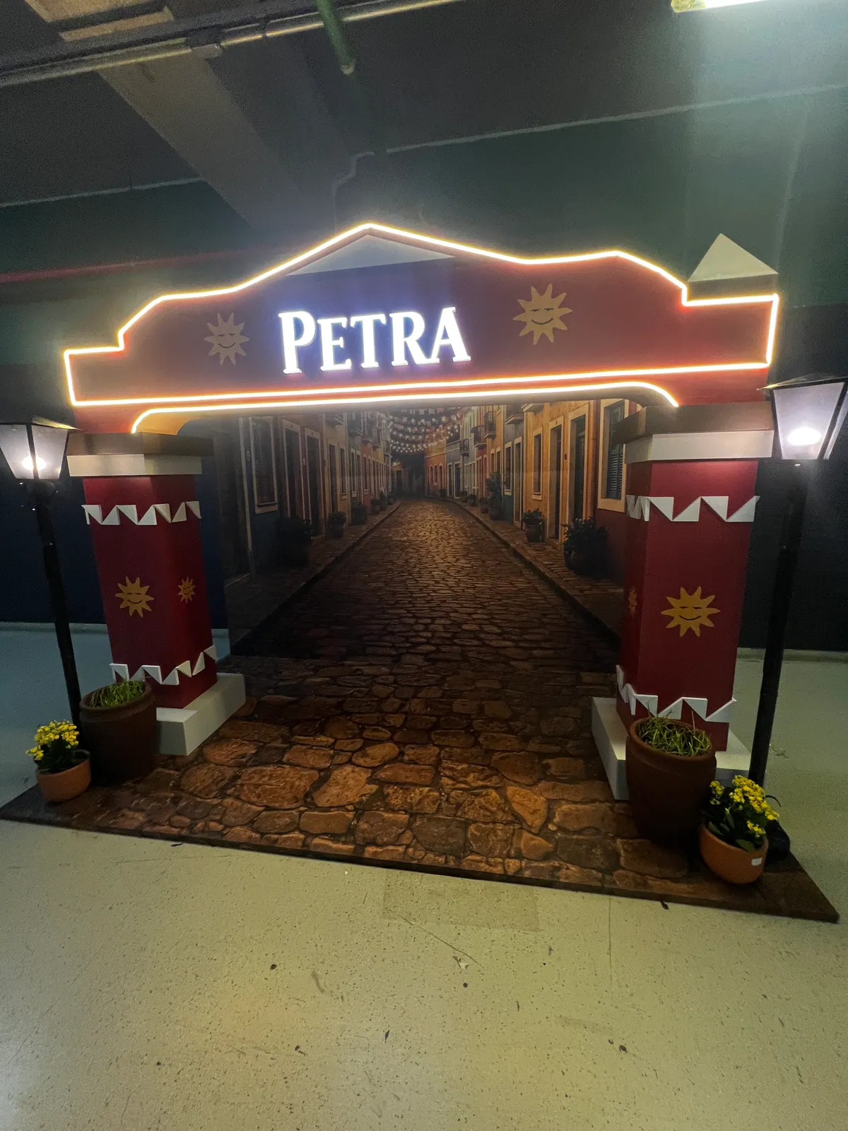 Ativação cenográfica da Petra em festival, com portal temático, bar e letreiros iluminados — foto 1