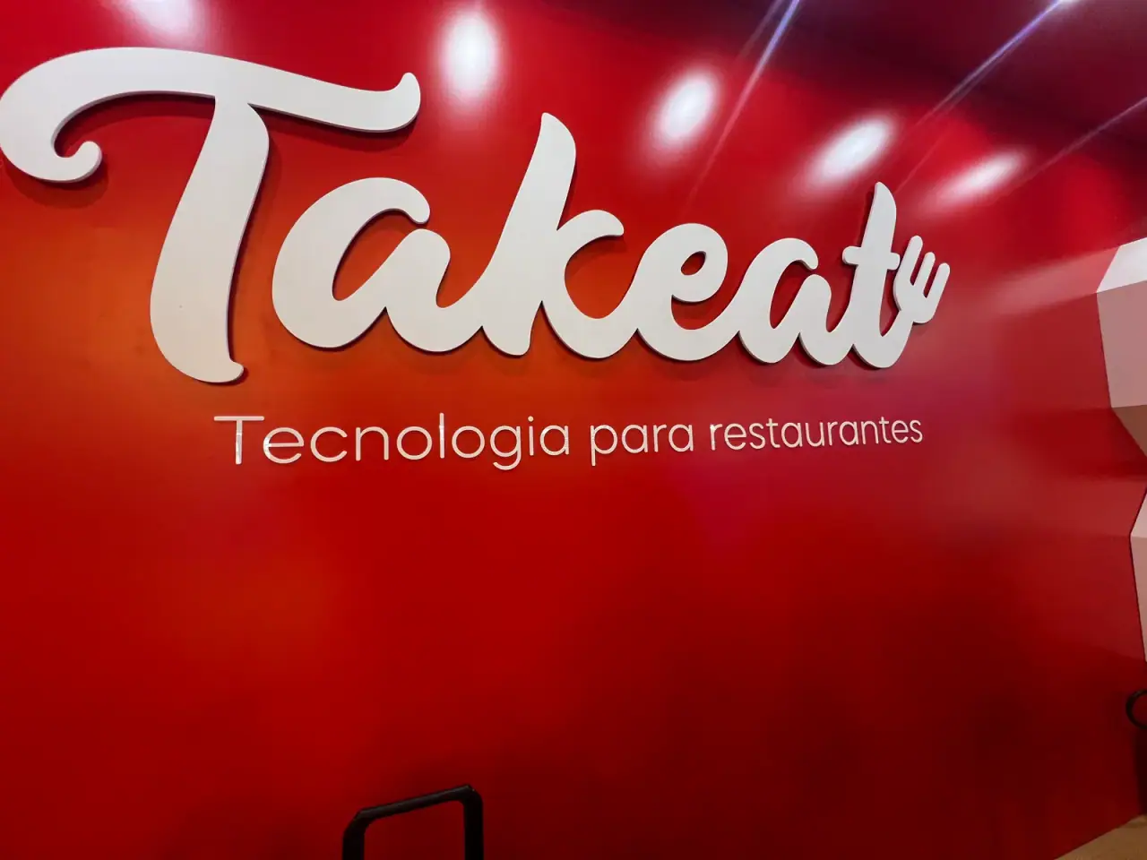 Stand da Takeat com logo em relevo sobre painel vermelho — foto 2