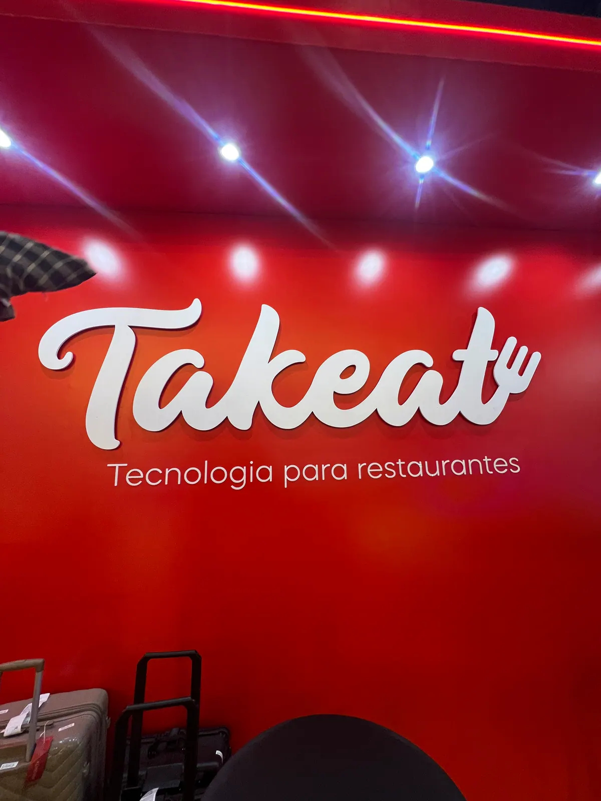 Stand da Takeat com logo em relevo sobre painel vermelho — foto 3